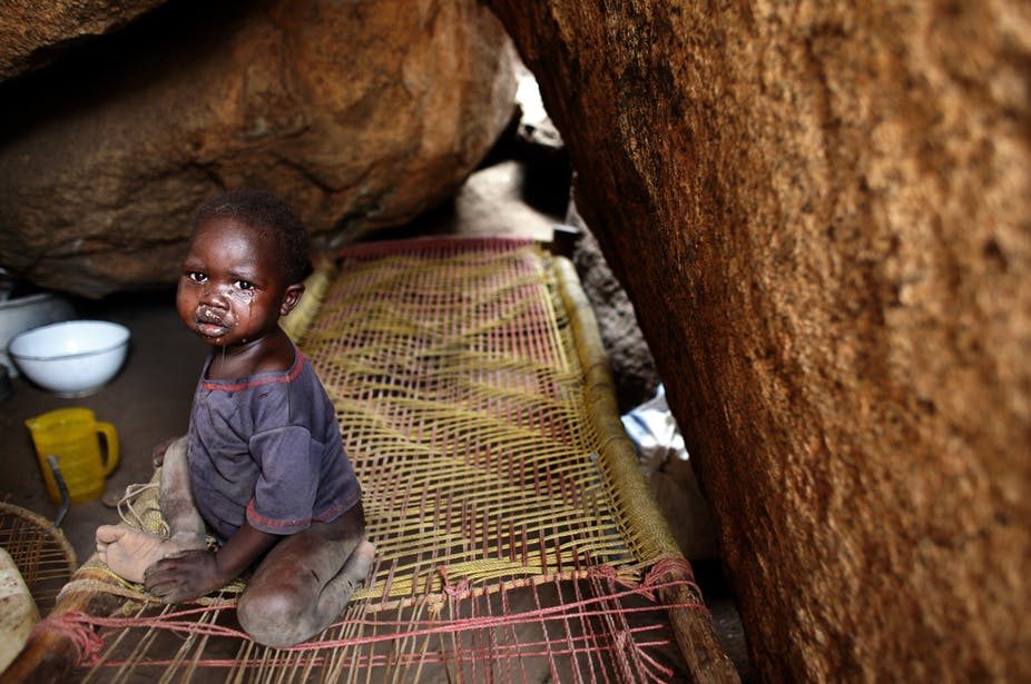 A malnourished child sits alone inside a cave shelter