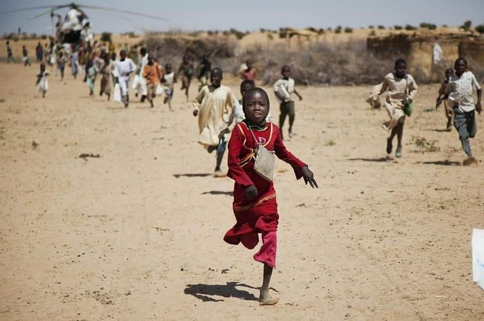 Children run toward an aid helicopter across open ground