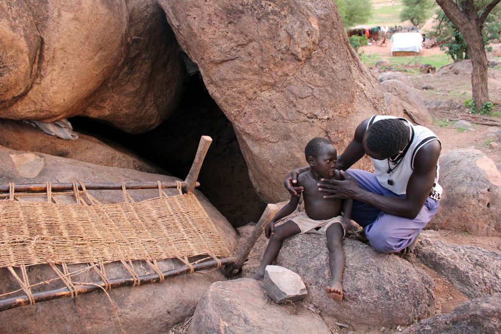 A father tends to his child outside a cave shelter