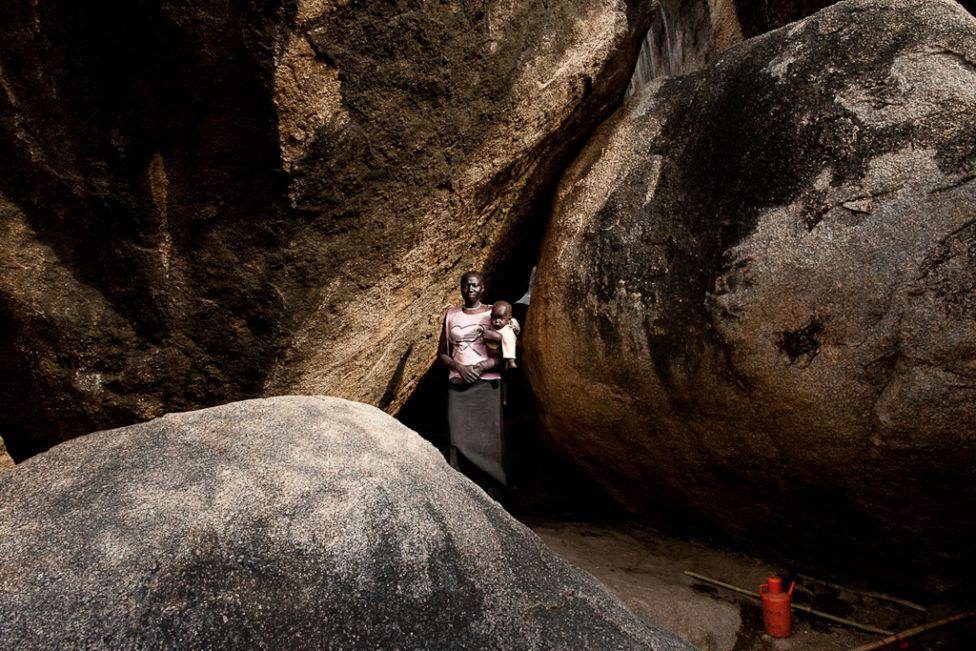 A mother holds her child at the mouth of a cave shelter